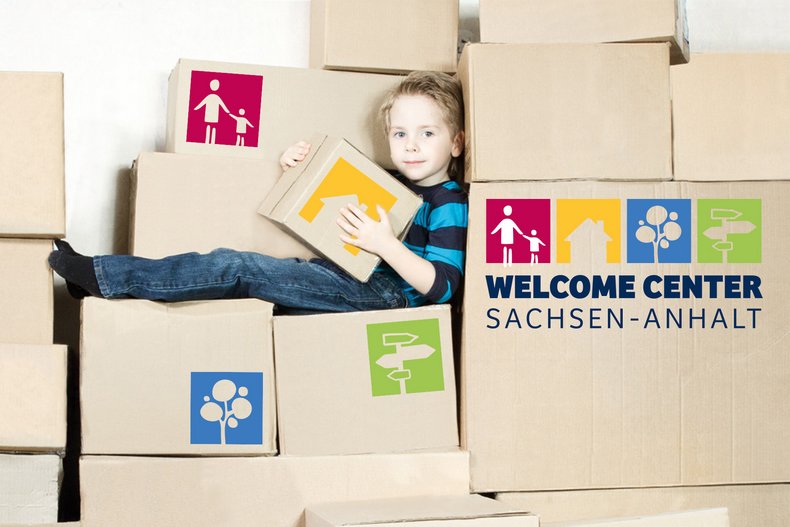 Ein kleiner Junge sitzt zwischen einer Vielzahl gepackter Kartons auf denen das Logo des WelcomeCenters Sachsen-Anhalt zu sehen ist.