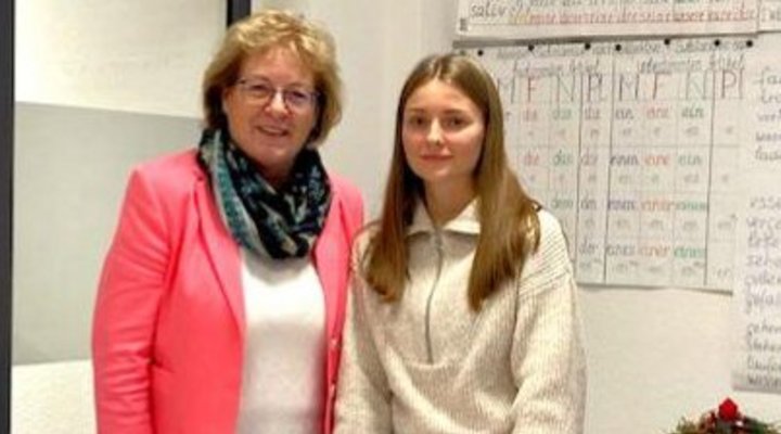 Zwei Frauen stehen an der Schulbank in einem Klassenzimmer vor einer voll beschriebenen Tafel