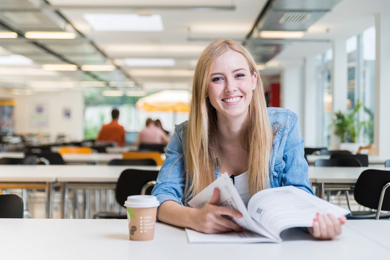 Eine junge Frau sitzt mit einer Fachzeitschrift an einem Schreibtisch