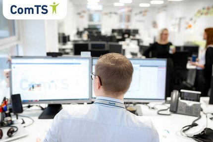 Zusehen ist ein junger Mann von hinten, der vor zwei Bildschirmen sitzt.